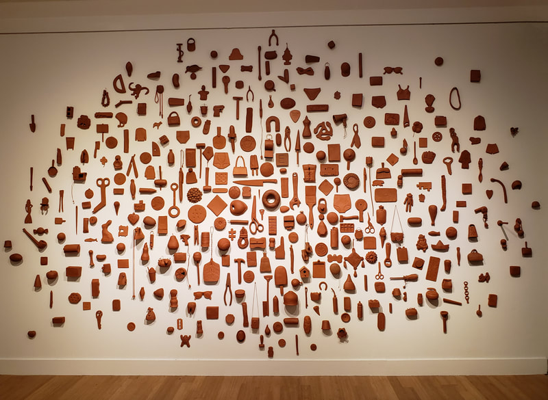 terra cotta objects hung on a white wall concentrated in the center and getting more dispersed further out from the center. 