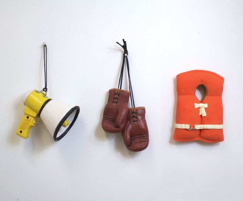 small scalled bullhorn, boxing gloves, and life vest made out of clay hanging on wall in that order. 