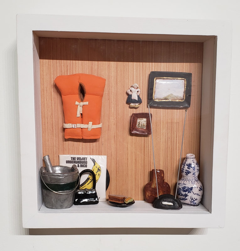 a grouping of miniaturized clay objects in a shadow box. 